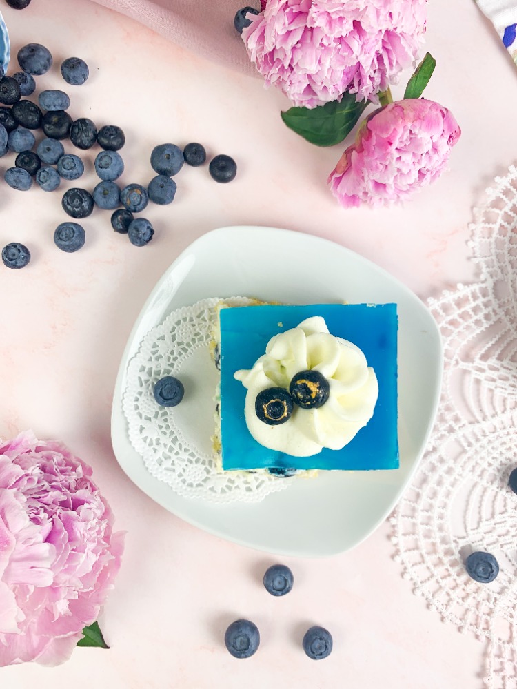 Das ist ein Bild von Blaubeer-Ecken mit Löffelbiskuitboden, Vanillecreme. Blaubeeren und einem blauen Tortengussspiegel.